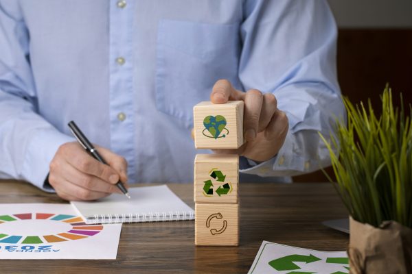 Homem empilhando blocos de madeira com símbolos de reciclagem e sustentabilidade, representando o conceito de economia circular no ambiente corporativo.