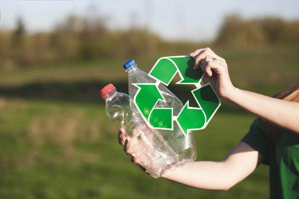 Pessoa segurando garrafas plásticas e símbolo de reciclagem, representando a logística reversa nas indústrias e práticas sustentáveis.